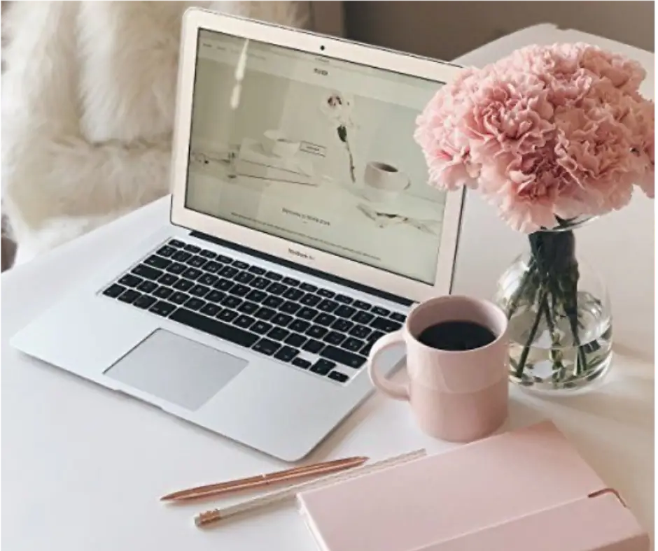 Photo of a laptop zoomed in on a website on a desk with pink peonies.