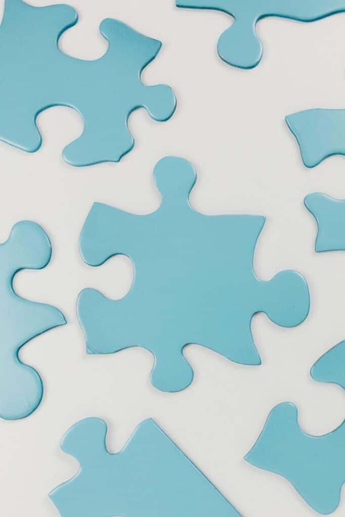 Close-up of blue puzzle pieces scattered on a white surface, conceptual and minimalistic.