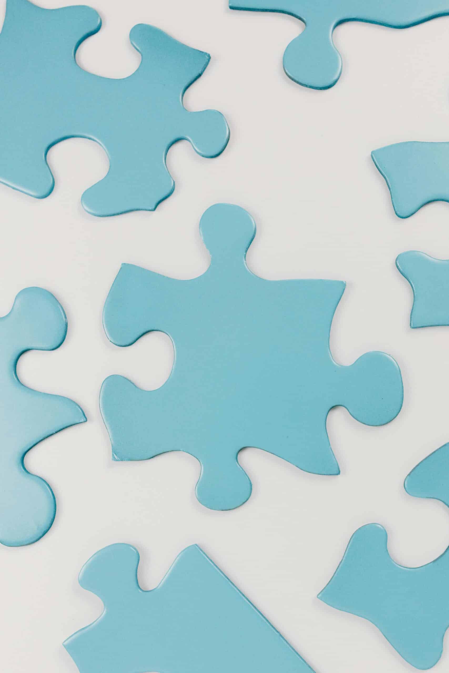 Close-up of blue puzzle pieces scattered on a white surface, conceptual and minimalistic.